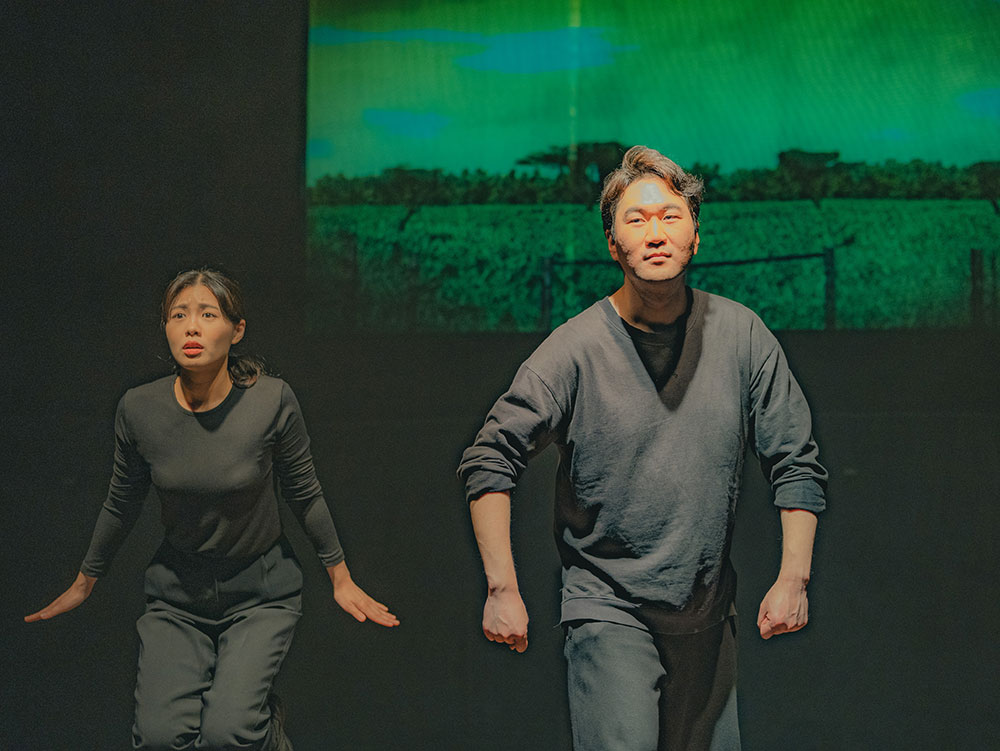 <긴긴밤>의 공연 사진. 한 남성 배우가 앞으로 걸어가는 듯한 포즈로 정면을 바라보고, 그 뒤에 양팔로 펭귄의 날개 모양을 본뜬 자세를 한 여성 배우가 엉거주춤하게 서 있다. 