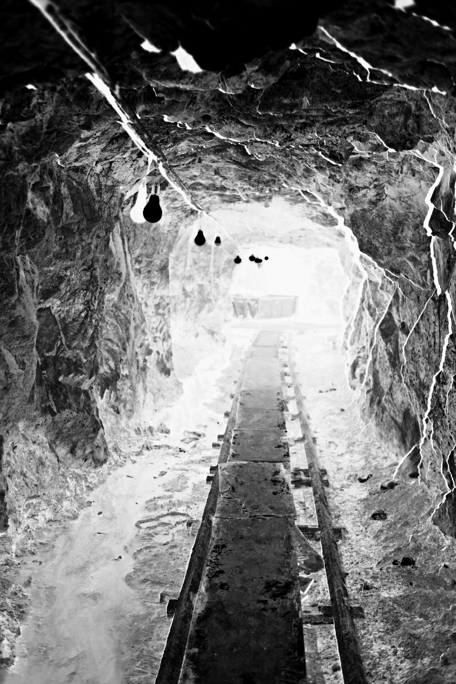 흑백 네거티브 기법을 활용하여 동굴 내부의 모습을 담아냈다. 중앙에 있는 목제 발판은 원경의 광원을 향해 뻗어 있으며, 천장에 일정한 간격으로 설치된 전구들은 공간의 깊이감을 강조한다. 네거티브 반전으로 인해 하얗게 묘사된 암벽의 균열은 독특한 시각적 효과를 제공한다. 터널 끝에서 보이는 빛은 폐쇄된 공간을 넘어 새로운 시작을 암시하고 있다. 